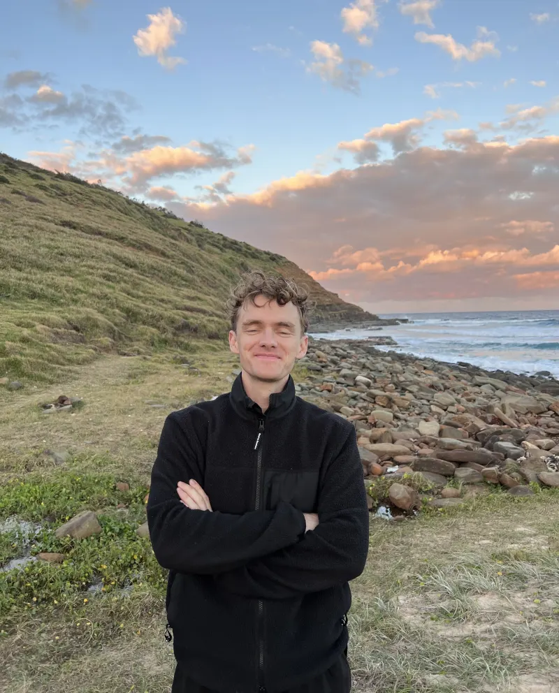 Kyle Redman standing on a rocky beach at sunset